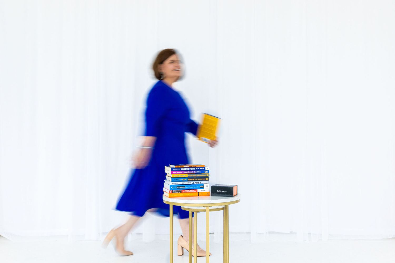 Vicki walking through a bright studio carrying a stack of books